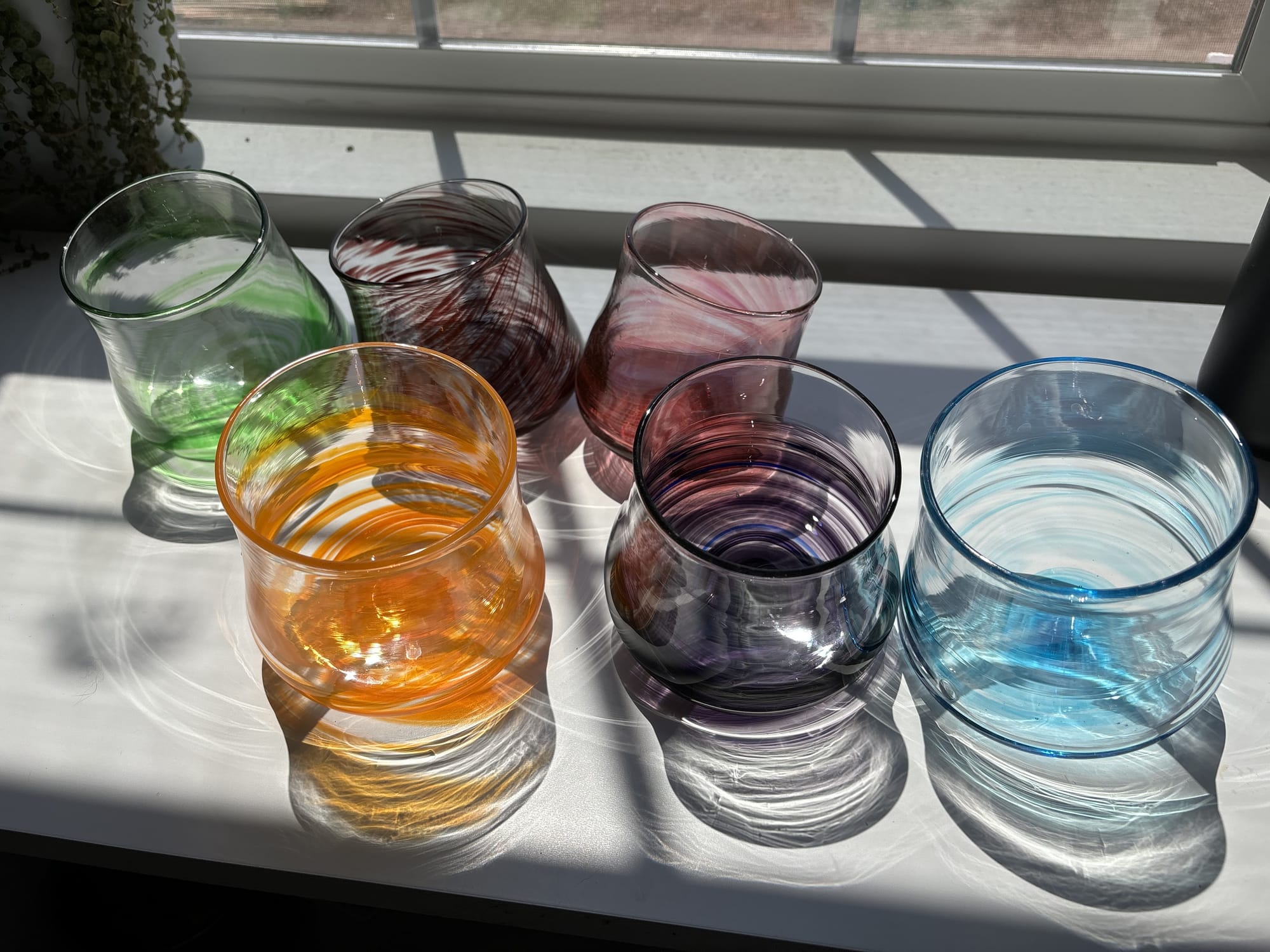 Handblown glasses in green, yellow, red, pink, purple, and blue with sunlight shining through them